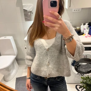 Stickad kofta med knappar - Mysig grå kofta med stora knappar framtill. Koftan har en v-ringad design och trekvartsärmar. Den är i jättebra skick!🥰