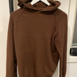 Cashmere Hoodie - Säljer en stilren brun hoodie från Oscar Jacobson i storlek M. Tröjan är tillverkad i en lyxig blandning av ull och kashmir, vilket gör den både varm och mjuk. Har ett litet hål på luvan men smälter in och syns ej då du har den på! :)