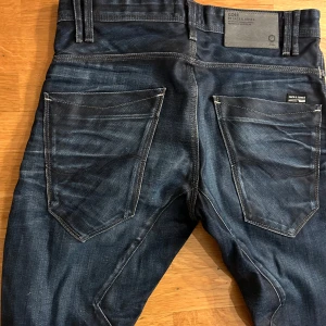 Mörkblå jeans från Jack & Jones - Snygga mörkblå jeans från Jack & Jones med en cool dragkedjedetalj på fickan. Byxorna har en knappgylf och klassiska femficksdesign och är sydda i sneda sömmar för bättre passform. Perfekta för en avslappnad stil.