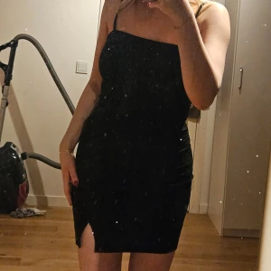 Glittrig klänning - Säljer denna klänning då det inte är min stil. Perfekt klänning till nyår då den är svart med massa skimmer! Så den glittrar lite. Den passar perfekt på kroppen och formar den fint. Den har en slit vid benet som ger klänningen en fin detalj!