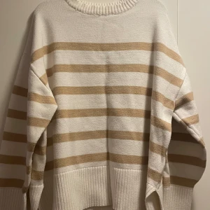 Randig beige och vit tröja - Säljer en supermysig randig tröja i beige och vit. Den har en avslappnad passform med långa ärmar och ribbade kanter. 🧡