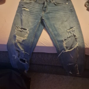 Blå jeans från Zara Woman - Säljer ett par snygga blå jeans från Zara Woman Premium Denim Collection. De har en cool, sliten look med flera revor och slitningar på benen. Perfekta för en avslappnad och trendig stil. Passar bra till både vardag och fest!