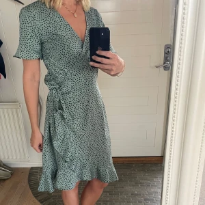 Grön prickig omlottklänning från ONLY - Säljer en superfin grön omlottklänning från ONLY med små svarta prickar. Klänningen har korta ärmar och en volangdetalj längst ner. Perfekt för vår och sommar! Den är i nyskick och passar både till vardags och fest. 💚