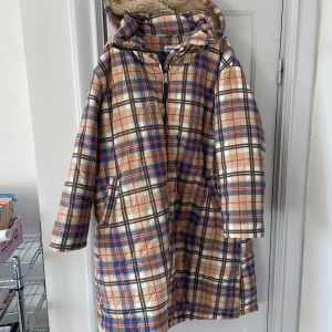 Rutig kappa från Weekday - Supercool vadderad kappa från Weekday. Köpt av Elsa Ekman. Teddyfoder i luvan och slits med knappar på vardera sida. 