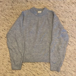 Grå stickad tröja - Säljer en mysig grå stickad tröja i bra skick. Perfekt för kyliga dagar med sin enkla och stilrena design. Tröjan har långa ärmar och ribbade kanter vid hals, ärmslut och nederkant. Passar både till vardags och lite finare tillfällen.