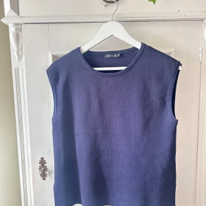 Mörkblå stickad väst från Stockh LM - Säljer en stilren mörkblå stickad väst från Stockh LM i storlek S. Perfekt för lager-på-lager under höst och vår. Västen har en enkel design med rund halsringning och är ärmlös, vilket gör den lätt att matcha med olika outfits. Den är i nyskick!