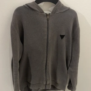 Grå hoodie från Guess - Säljer en snygg grå hoodie från Guess i storlek XS. Den har en dragkedja framtill och Guess-loggan på ärmarna. Perfekt för en casual look och passar bra till både höst och vår. Den är i bra skick och superbekväm! Obs! Passar också storlek S, 9/10