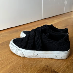 Svarta sneakers med kardborreband - Säljer ett par svarta sneakers med vit sula och kardborreband. De är lite smutsiga men i bra skick. Perfekta för vardagsbruk och superbekväma!