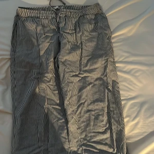 Randiga byxor med snörning - Säljer ett par bekväma randiga byxor i blå och vitt. Byxorna har en avslappnad passform med snörning i midjan för justerbarhet. Perfekta för en casual look.