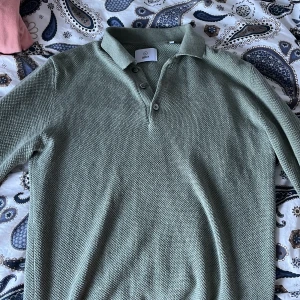 Grön pikétröja från Bläck - Snygg grön pikétröja från Bläck i en skön textur. Tröjan har en klassisk krage med knappar och långa ärmar. Perfekt för en stilren look.