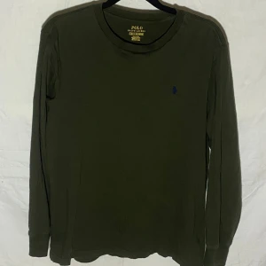Olivgrön långärmad tröja från Polo Ralph Lauren - Säljer en stilren olivgrön långärmad T-shirt från Polo Ralph Lauren. Tröjan har en diskret broderad logotyp på bröstet och är tillverkad i ett mjukt bomullsmaterial. Perfekt för en avslappnad och snygg look. Storlek L 14-16år så motsvarar typ S i vuxen