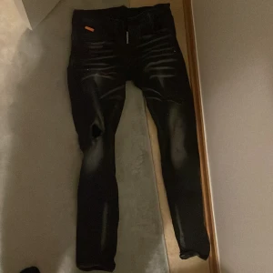 Svarta jeans med slitningar - Snygga svarta jeans med coola slitningar och en tight passform. Perfekta för en trendig look. De har en klassisk design med fem fickor och knappgylf. DSQ