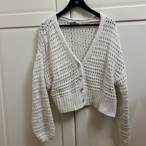 Vit stickad kofta med knappar - Säljer en söt vit stickad kofta med v-ringning och knappar framtill. Koftan har en luftig stickning och är croppad med långa ärmar. Perfekt för lager-på-lager-stil!