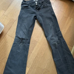 Svarta  jeansbyxor med knappar från Gina young (Pris kan diskuteras) - Snygga grå jeansbyxor med bootcut-stil och knappar fram. Byxorna har en klassisk design med fickor bak och en bekväm passform. Perfekta för en avslappnad look.