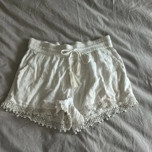 Vita spetsshorts från Object - Snygga vita shorts från Object med spetsdetaljer längs kanterna och en bekväm resårmidja med knytband. Perfekta för varma sommardagar!