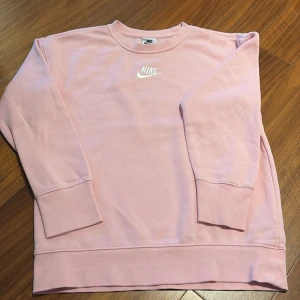 Rosa sweatshirt från Nike - Säljer en snygg rosa sweatshirt från Nike med deras klassiska logga broderad i vitt på bröstet. Tröjan har långa ärmar och en bekväm passform. Köpt från stadium.