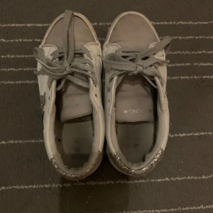 Vita sneakers med stjärndetaljer - Snygga vita sneakers med glittriga detaljer och stjärnor på sidan. Skorna har snörning och en bekväm passform. Perfekta för en trendig look.