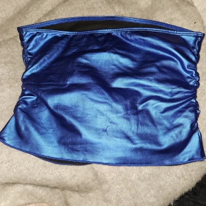 Blå tubtopp nytt - Nytt En blå, blank tubtopp med en elastisk kant. Toppen är utan axelband. Tyvärr är lappen bortklippt men det är strl M