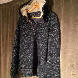 Stickad hoodie med fodrad luva - Säljer en mysig mörkblå stickad hoodie med vitmelerat mönster och knappar vid halsen. Den har en fodrad huva med mjukt material och långa ärmar. Perfekt för kyliga dagar! Vid minsta fråga eller fundering hör av er🤝