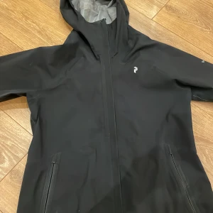 Svart vindjacka från Peak Performance - Säljer en stilren svart vindjacka från Peak Performance. Jackan har en praktisk huva och dragkedja framtill. Perfekt för blåsiga dagar och regn.