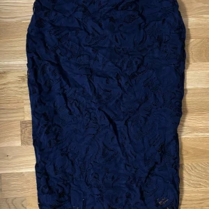 Mörkblå spetskjol från H&M - Elegant mörkblå kjol i spets från H&M. Kjolen har ett vackert mönster och är perfekt för en stilfull look. Den är knälång och har en smickrande passform.