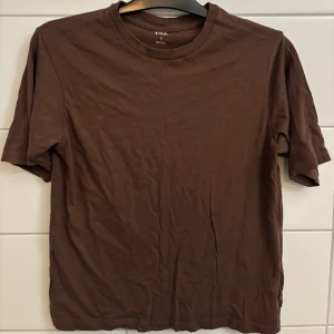 Brun t-shirt från Lager 157  - Säljer en enkel brun t-shirt från Lager 157. Den har en normal passform och är kortärmad, perfekt för vardagsbruk. Tillverkad i mjukt bomullsmaterial för en bekväm känsla.