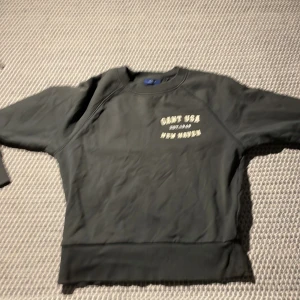Mörkgrå sweatshirt från GANT - Snygg mörkgrå sweatshirt från GANT med tryck 'GANT USA EST. 1949 NEW HAVEN' på bröstet. Tröjan har långa ärmar och en rund halsringning. Perfekt för en avslappnad stil.