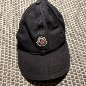Svart keps från Moncler - Snygg svart keps från Moncler med broderad logotyp framtill. Kepsen har en justerbar rem baktill för perfekt passform. Perfekt för en stilren look.