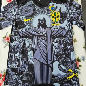 Unik fotbollströja med Kristusmotiv - Snygg och unik fotbollströja från Nike med ett iögonfallande motiv av Kristusstatyn i Rio de Janeiro. Tröjan har korta ärmar och är designad i svart och grått med gula detaljer, inklusive CBF-emblemet och Nike-loggan. Perfekt för fotbollsfans som vill sticka ut!