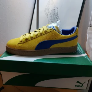Puma suede - Snygga gula sneakers från Puma med blå detaljer och en brun sula. Skorna har snörning och är tillverkade i mocka. Perfekta för en sportig look.