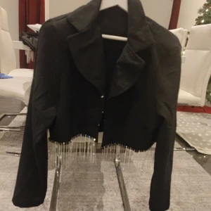 Svart croppad jacka med pärlor och kjol - Snygg svart croppad jacka med långa ärmar och pärldetaljer längs nederkanten. Perfekt för att ge en extra touch till din outfit och kjol med pärldetaljer 