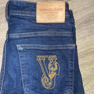 Blå jeans från Versace Jeans Couture - Snygga blå jeans från Versace Jeans Couture med ett stilrent broderat V på bakfickan. Jeansen har en klassisk design med en läderpatch på baksidan av midjan. Perfekta för en trendig look.