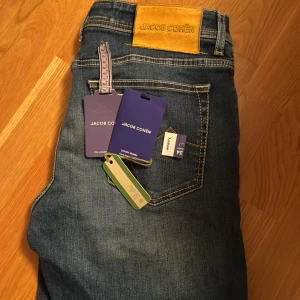 Blå jeans från Jacob Cohen - Snygga blå jeans från Jacob Cohen med klassisk femficksdesign och knappgylf. Jeansen har en stilren look med subtila detaljer och en bekväm passform. Perfekta för en avslappnad stil. Nypris ca 6000kr säljer för 1495. 