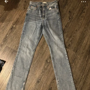 Blå jeans från Gina Tricot - Säljer ett par klassiska blå jeans från Gina Tricot. De har en hög midja och en straight passform. Jeansen har en dragkedja och knapp framtill samt traditionella fem fickor. Perfekta för en avslappnad stil.