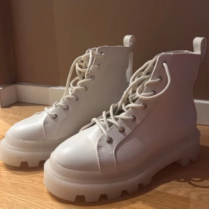 Vita boots från H&M Divided - Snygga vita boots från H&M Divided i veganskt material. De har en rejäl sula och snörning framtill. Skorna är i storlek 38 med prislappen kvar då de aldrig är använda. 