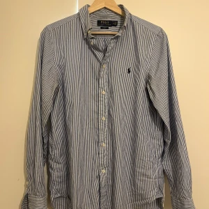 Randig skjorta från Polo Ralph Lauren - Snygg och näst intill oanvänd Ralph Lauren skjorta. Skjortan passar till allt och är i nyskick. Säljer på grund av att jag växt ur den. Vid frågor är det bara att höra av sig! 