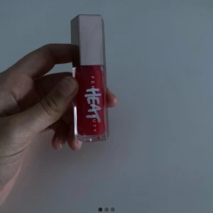 Fenty Beuty Heat Lip Gloss i cherry heat  - Fenty heat gloss i cherry. Den blir INTE röd på läpparna utan får en väldigt fin rosa färg. har ENBART använt 1 gång, så den är väldigt fräsch och i bra skick