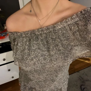 Set från neo noir - Charmigt set med ett blommigt mönster i beige och svart. Setet består av en off-shoulder top och en kjol med volanger och en smockad överdel för en bekväm passform. Perfekt för sommarens varma dagar.