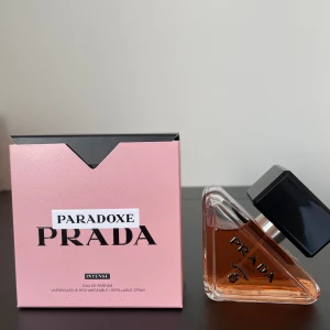 Paradoxe Intense Eau de Parfum från Prada - Elegant och modern parfym från Prada, Paradoxe Intense, med en unik trekantig glasflaska och svart lock. Endast ett fåtal sprayer används. Förpackningen är snygg rosa med svart text. En doft som utstrålar lyx och intensitet.
