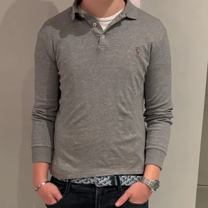 Grå pikétröja från Ralph Lauren - Säljer en stilren grå pikétröja från Ralph Lauren i Storlek S, sitter mer som XS. Jag på bilden är 175 och väger 66 kg. Topp skick! Hör av er!!🙌🏼