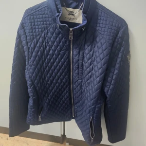 Blå quiltad jacka från Burberry Brit - Snygg blå quiltad jacka från Burberry Brit med dragkedja framtill och hög krage. Jackan har långa ärmar och en stilren design med diskreta detaljer. Perfekt för kyligare dagar.👌