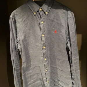 Mörkblå skjorta från Ralph Lauren - Snygg mörkblå skjorta från Ralph Lauren med klassisk krage och knappar framtill. Skjortan har en broderad logotyp i rött på bröstet och är tillverkad i ett bekvämt material. Perfekt för en stilren look.