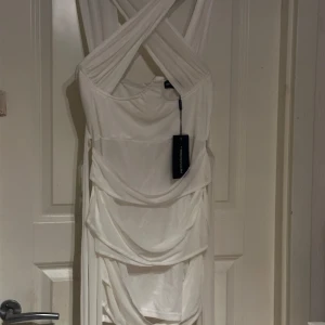 Vit klänning från PrettyLittleThing - Elegant vit klänning med korsade axelband och draperad design från PrettyLittleThing. Perfekt för en stilren look.