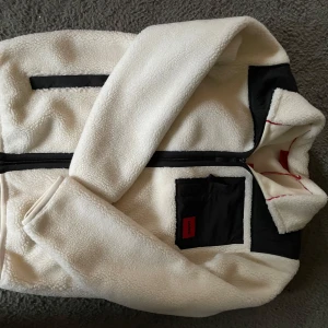Vit fleecejacka från Hugo - Säljer en stilren vit fleecejacka från Hugo med svarta detaljer. Jackan har en dragkedja framtill och en praktisk ficka på bröstet. Perfekt för kyliga dagar. Det är helt oanvänd 