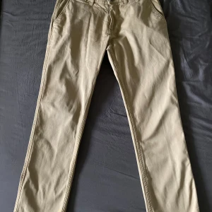 Beige chinos - Säljer ett par snygga beige chinos i normal passform. Perfekta för både vardag och lite mer uppklädda tillfällen. De har en klassisk design med fickor fram och bak, och är gjorda i ett bekvämt bomullsmaterial. Passar perfekt till höst- och vårgarderoben!