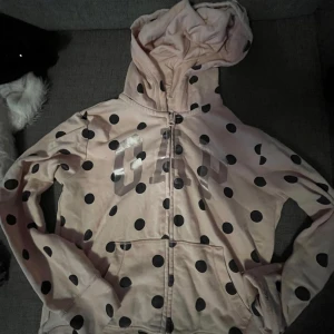Rosa prickig hoodie från GAP  - Säljer en superfin rosa hoodie från GAP  med stora svarta prickar. Den har en dragkedja framtill och en mysig huva. Perfekt för både lek och mysiga dagar hemma! Passar både i XS och XXS