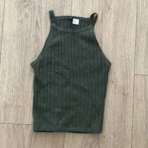 Grön ribbad linnetopp från H&M - Säljer en snygg grön ribbad linnetopp från H&M:s Divided-kollektion. Perfekt för sommardagar eller som ett lager under en jacka. Toppen har en tight passform och är i mycket bra skick. Passar både till vardags och fest!