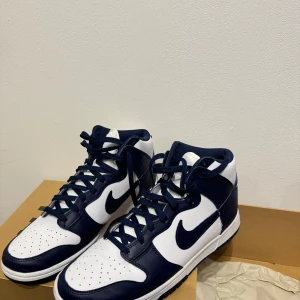 Nike Dunk i marinblått och vit - Säljer ett par Nike Dunk sneakers i marinblått och vit. De är i nytt skick och har en klassisk design med snörning. Perfekta för både vardag och fest.