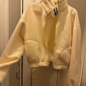 Ljus gul fleecejacka från Gymshark - Mysig beige fleecejacka från Gymshark i storlek XS. Jackan har en dragkedja framtill och är croppad för en modern look. Perfekt för kyliga dagar när du vill vara både varm och stilren. 🧥✨
