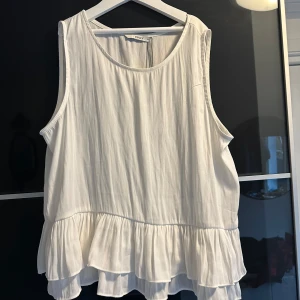 Vit ärmlös topp från ONLY - Säljer en söt vit ärmlös topp från ONLY i storlek 36. Toppen har en volangdetalj vid nederkanten som ger en romantisk touch. Perfekt för sommardagar eller en avslappnad vårlook. Materialet är lätt och luftigt, vilket gör den bekväm att bära.